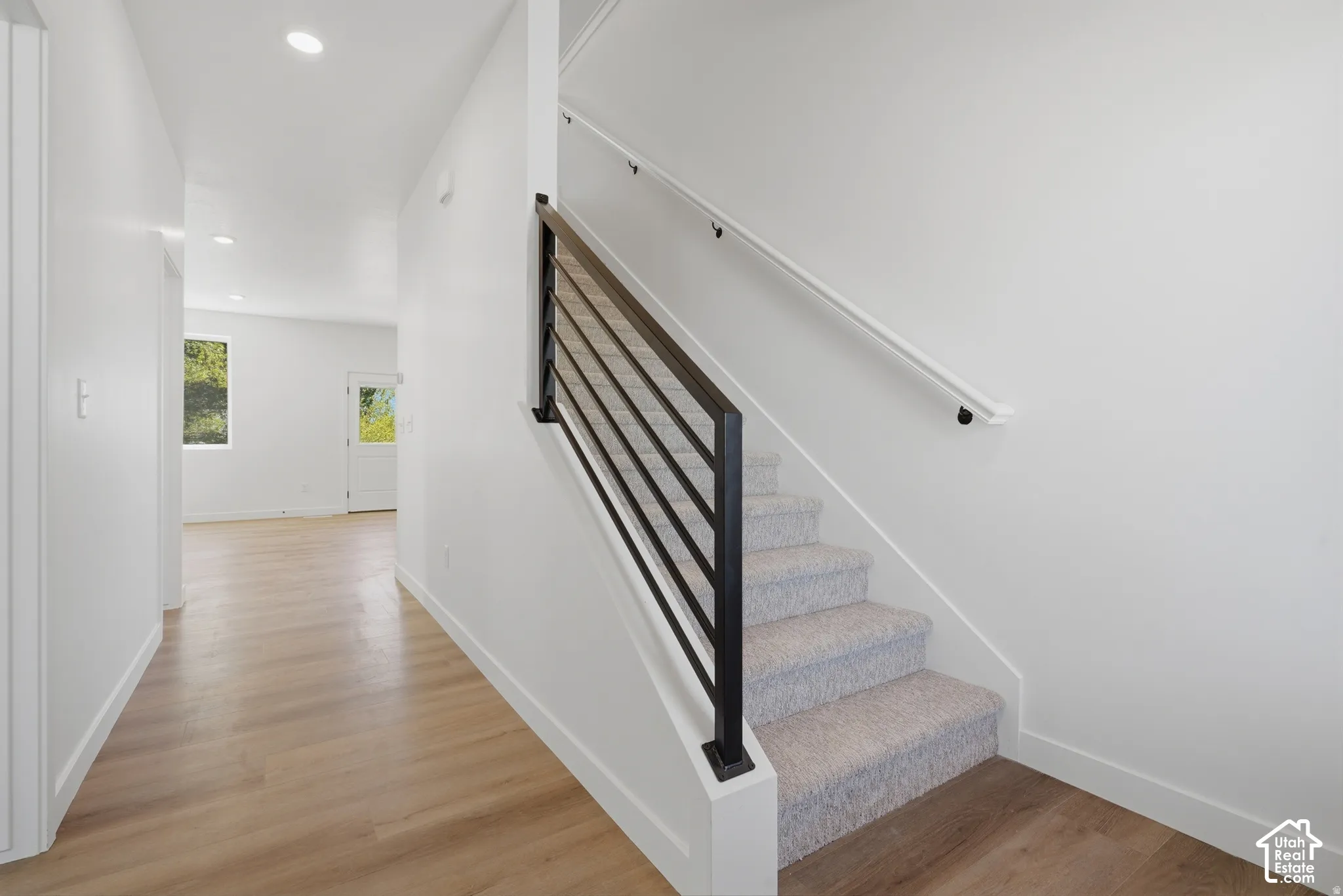 Staircase with carpeted treads and contemporary metal railing, light wood-finish flooring, recessed lighting, and white walls