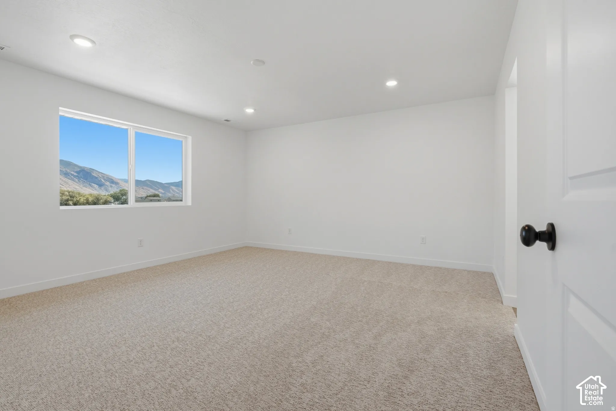 Neutral tone wall paint, recessed ceiling lighting, light-toned carpet, white trim, and a mountain backdrop