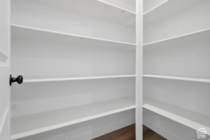 Walk-in pantry featuring multiple white shelves and wood-finish flooring