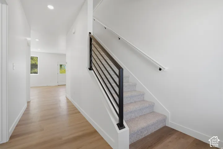 Staircase with carpeted treads and contemporary metal railing, light wood-finish flooring, recessed lighting, and white walls