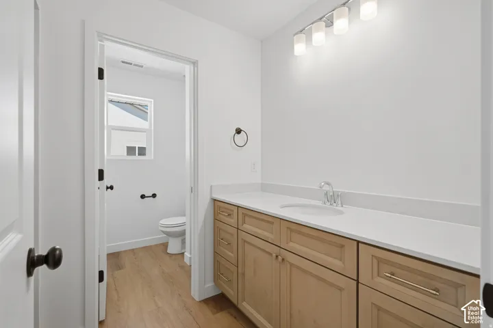 Wood-finish flooring, light-toned vanity with multiple cabinets and drawers, white countertop with an integrated sink, and an overhead four-light fixture
