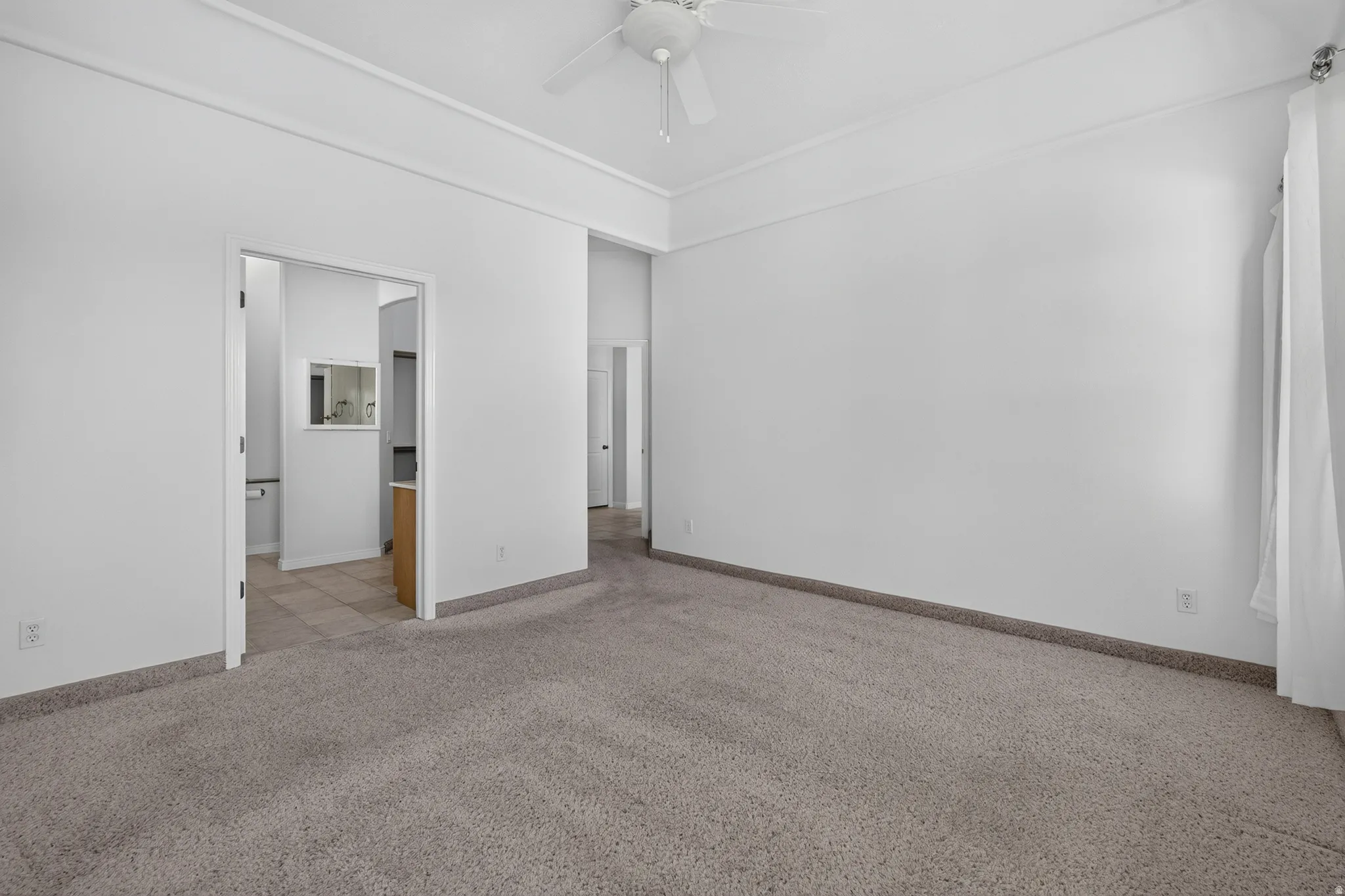 Spacious room featuring neutral carpeting, white walls, and a ceiling fan