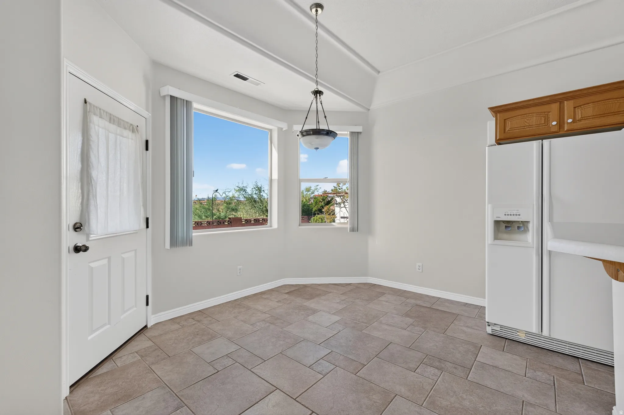 Angled tile flooring, multiple windows, vaulted ceiling, and pendant light fixture