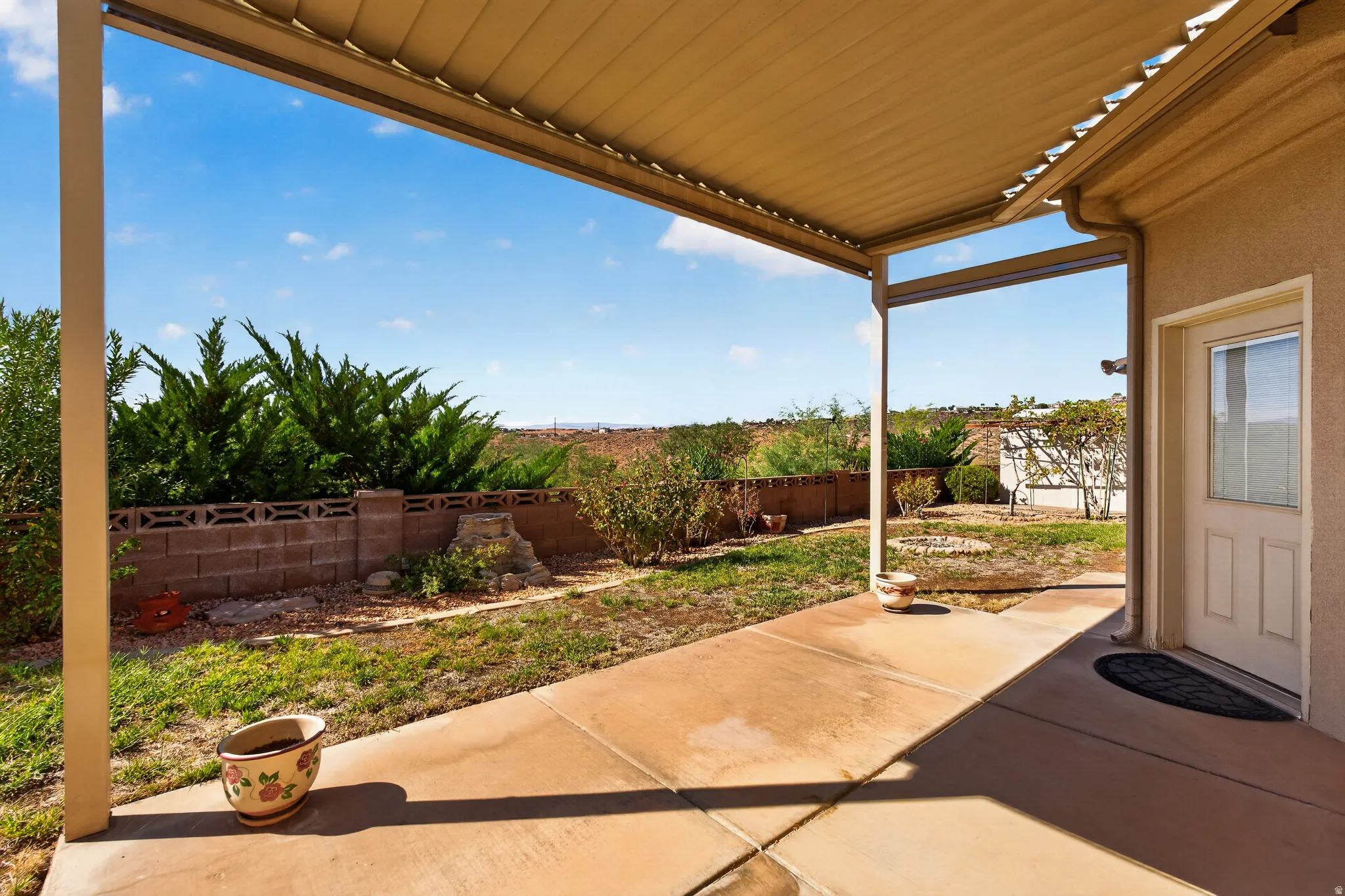 Covered patio with a concrete slab, stucco exterior, and a glass-paneled entry door, remote blinds.