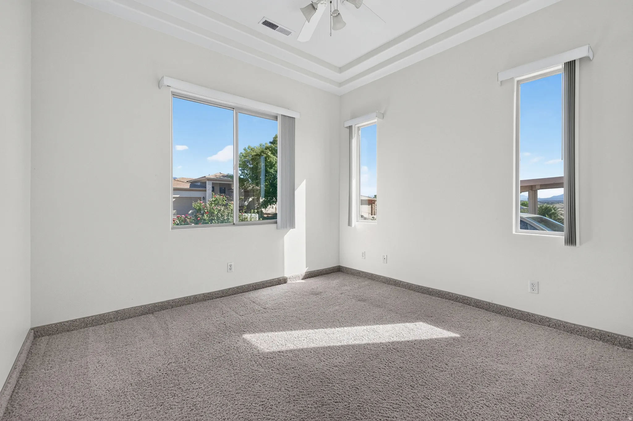 Recessed ceiling with layered trim, multiple windows, and a ceiling fan