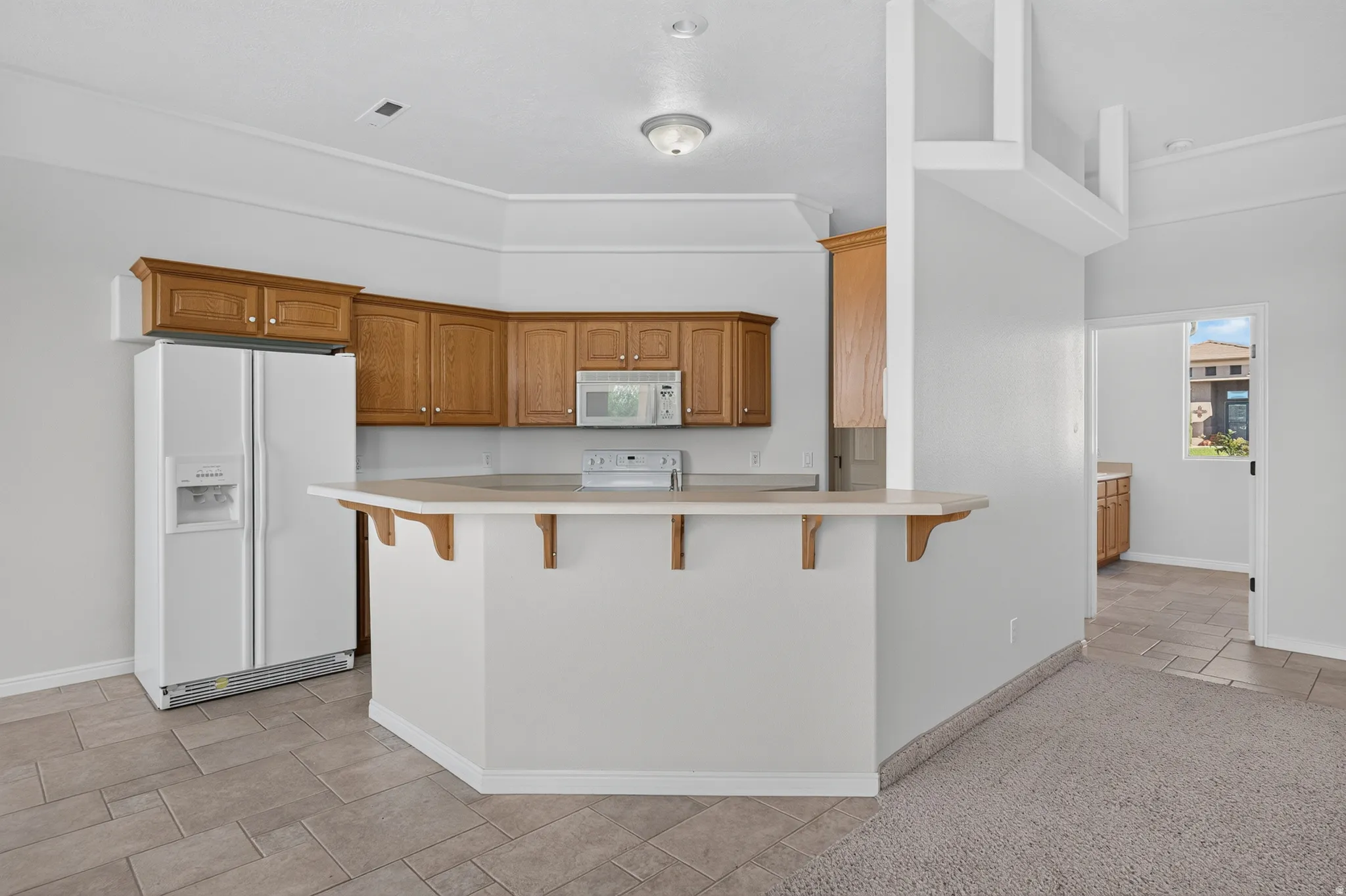 Kitchen featuring wood cabinetry, white appliances, a peninsula with counter seating, and tile flooring