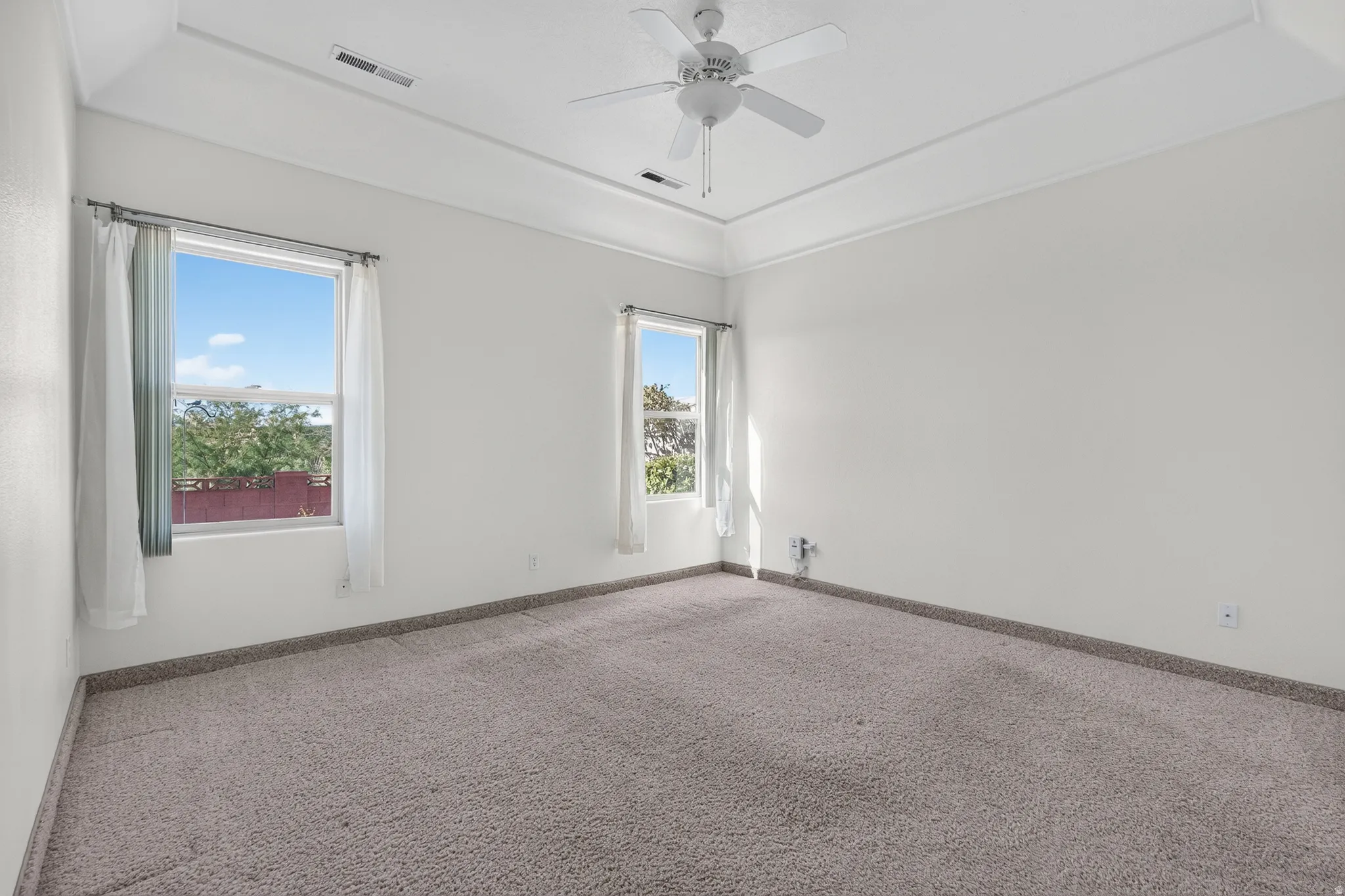 Spacious room featuring neutral carpeting, a tray ceiling, and a ceiling fan