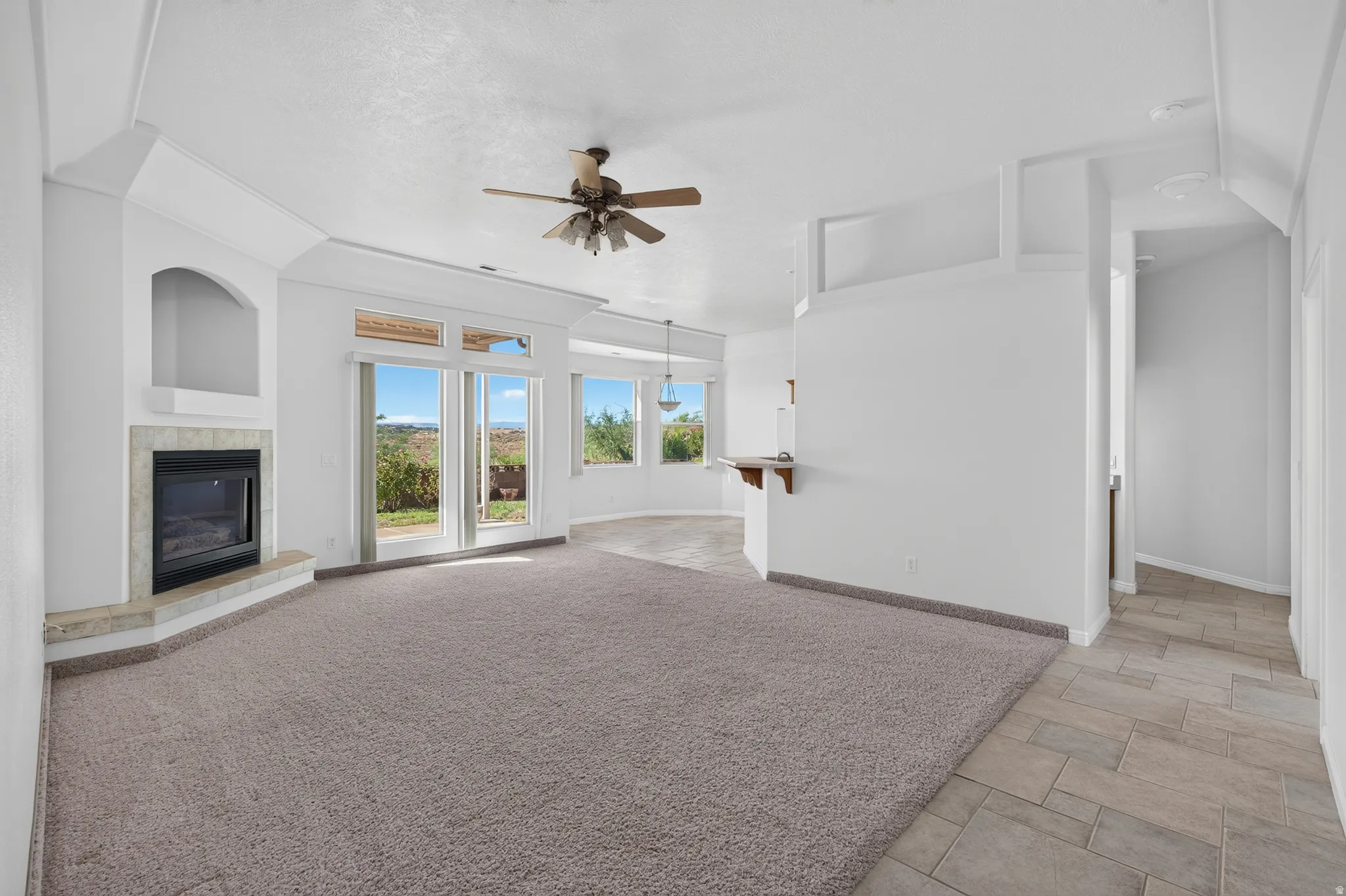 Carpeted living area with a built-in fireplace, arched alcove, ceiling fan, and sliding glass doors