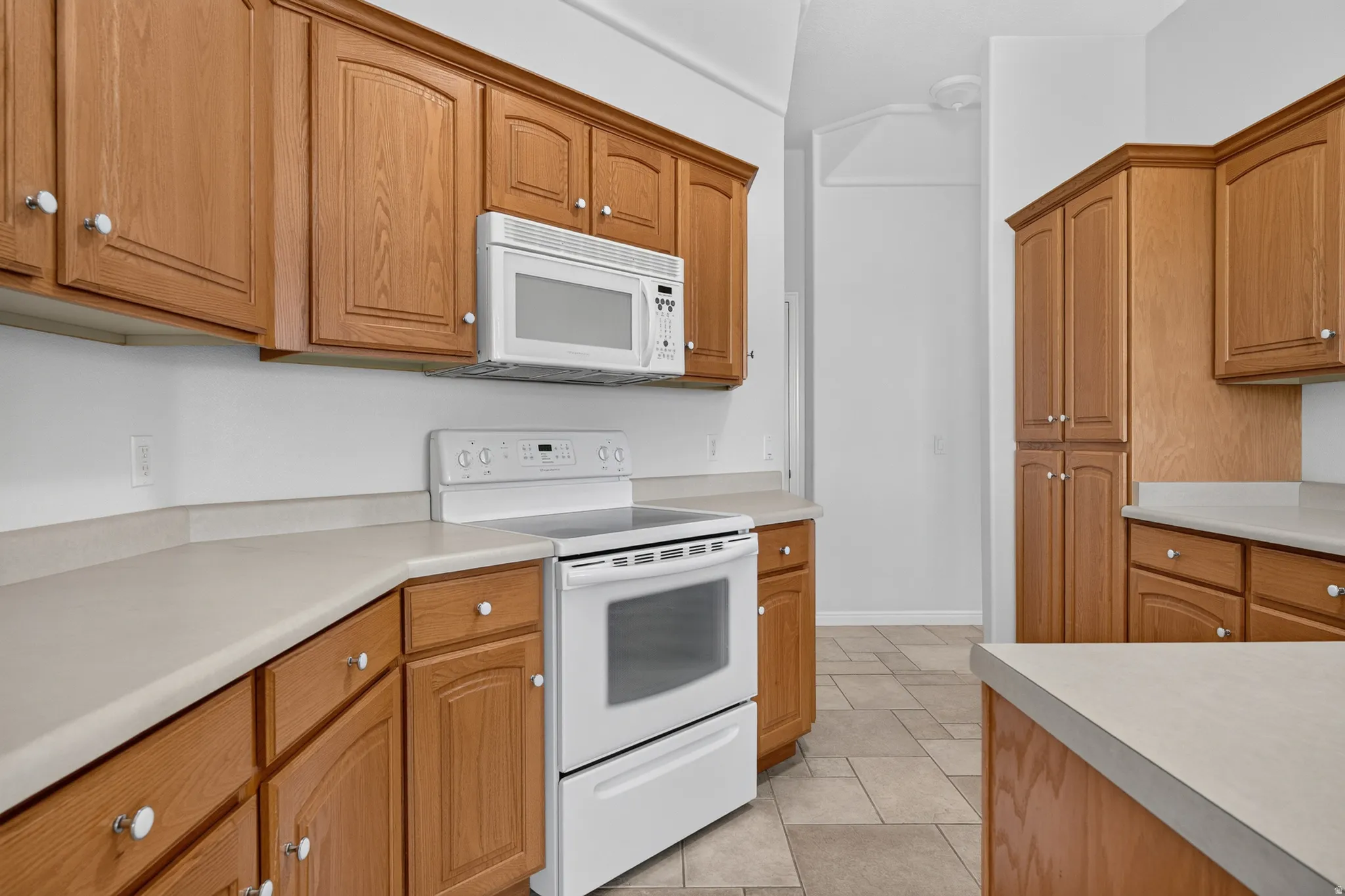 Kitchen featuring wood cabinetry, light-toned countertops, white appliances, and tiled flooring