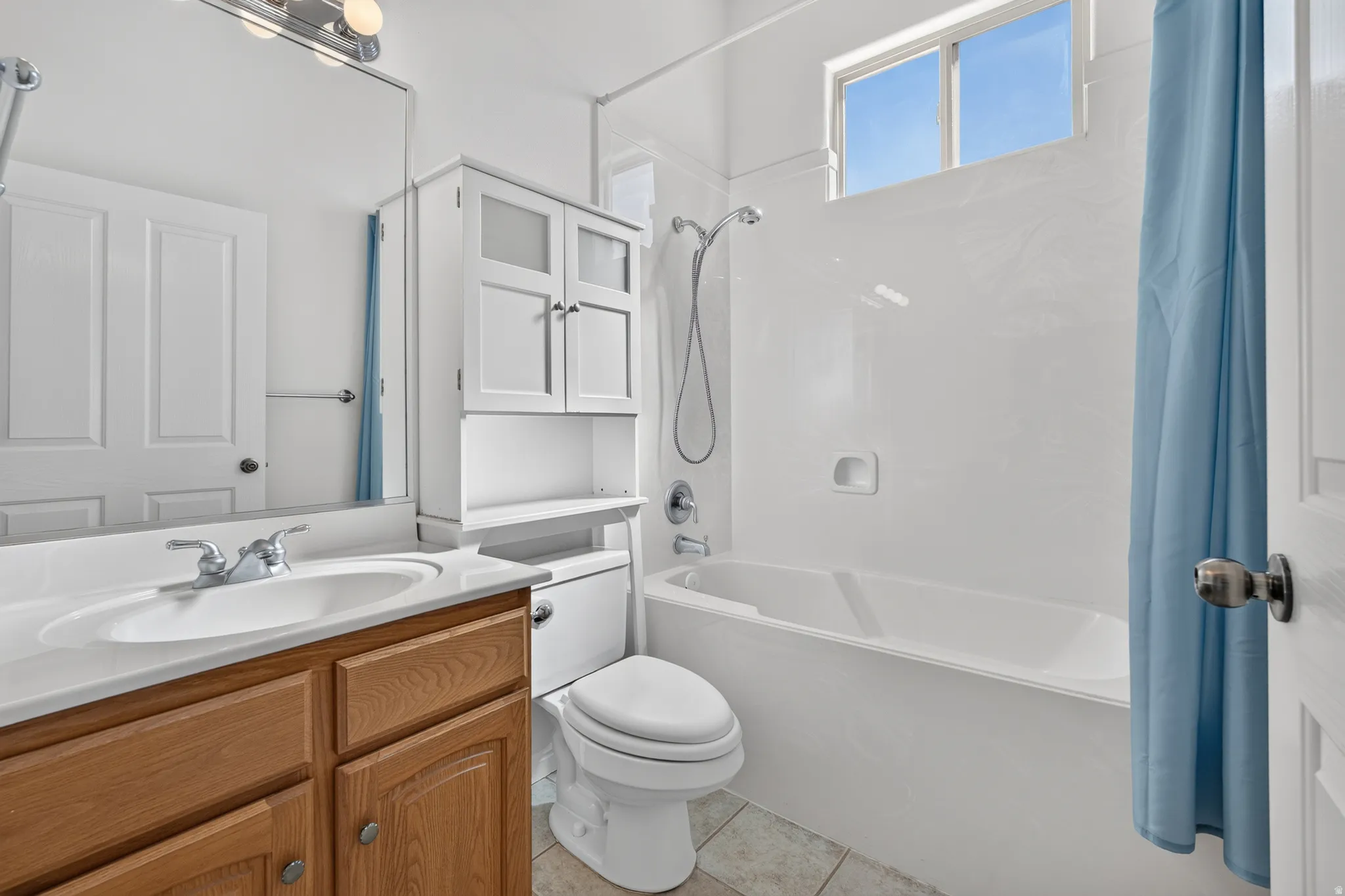 Built-in wood-finish vanity with an integrated sink and chrome faucet, white over-toilet storage cabinetry, and a bathtub with a shower fixture