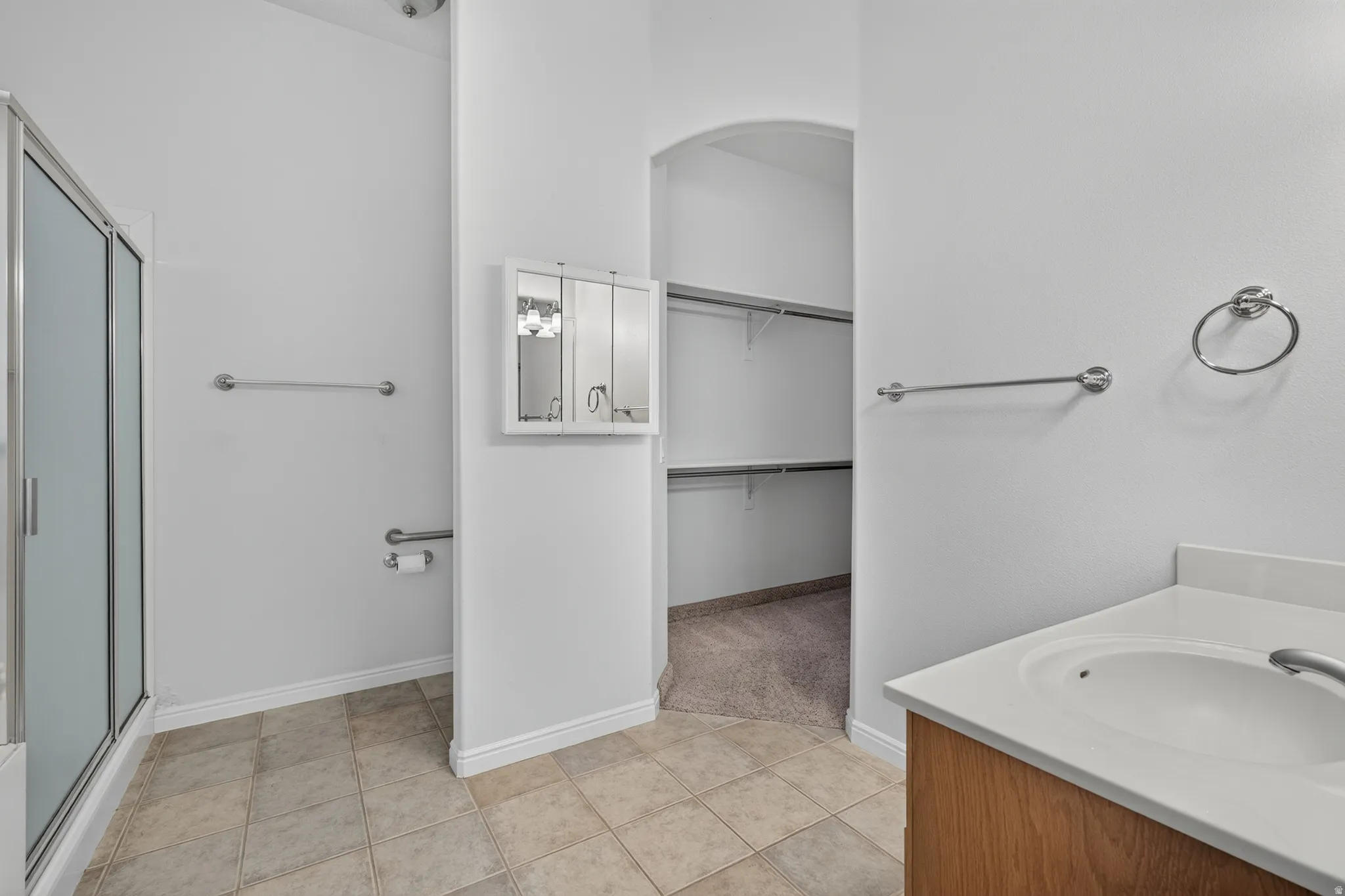 Glass-enclosed shower, built-in medicine cabinet, arched doorway, vanity with integrated sink, and tile flooring