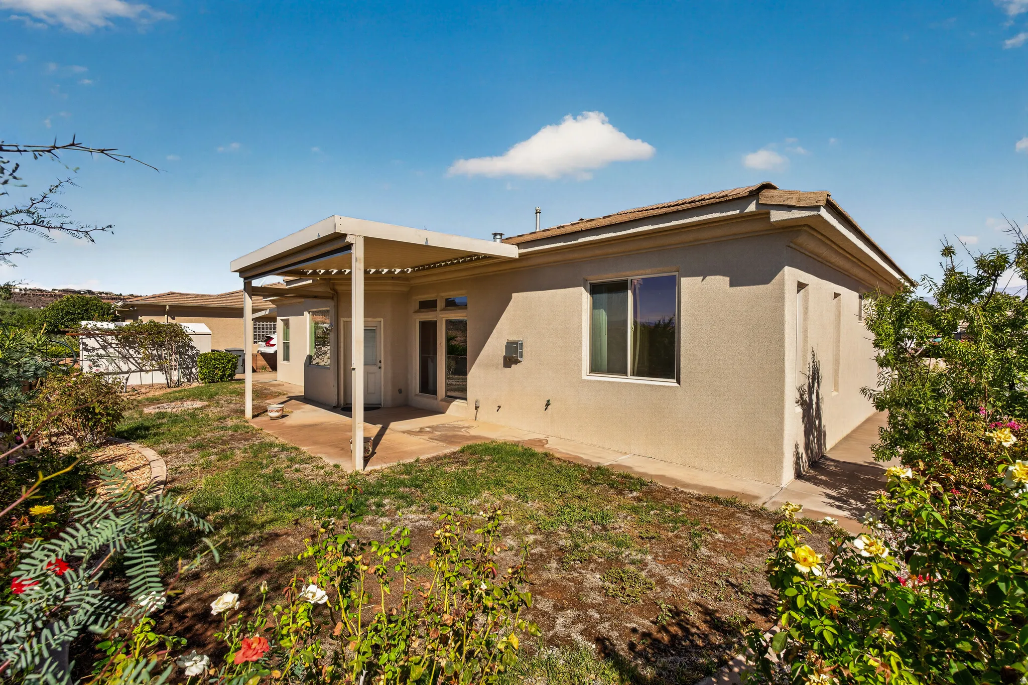 Rear exterior featuring a patio cover, remote blinds, stucco siding, and multiple windows
