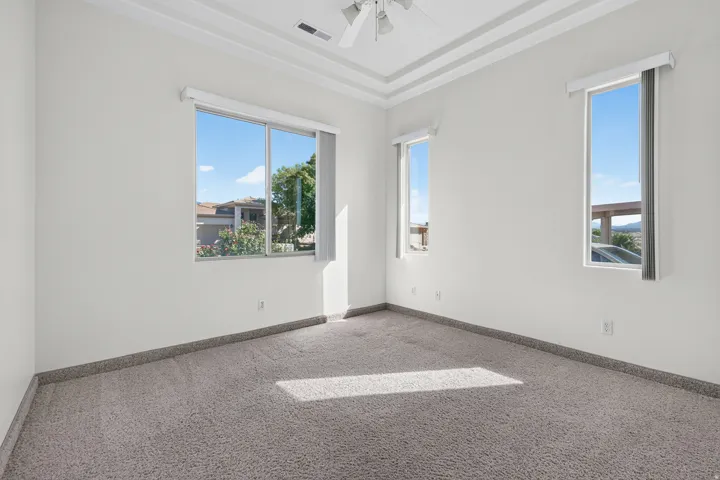 Recessed ceiling with layered trim, multiple windows, and a ceiling fan