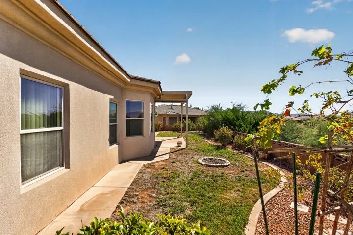 Exterior stucco finish, multiple windows, concrete walkway, terraced landscaping, and a fire pit area, fruit trees