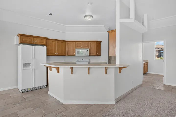 Kitchen featuring wood cabinetry, white appliances, a peninsula with counter seating, and tile flooring