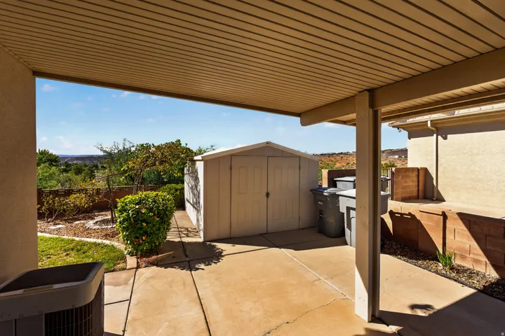Carport with a concrete surface, a built-in storage shed, and a retaining wall