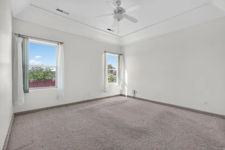 Spacious room featuring neutral carpeting, a tray ceiling, and a ceiling fan