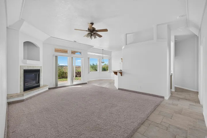 Carpeted living area with a built-in fireplace, arched alcove, ceiling fan, and sliding glass doors
