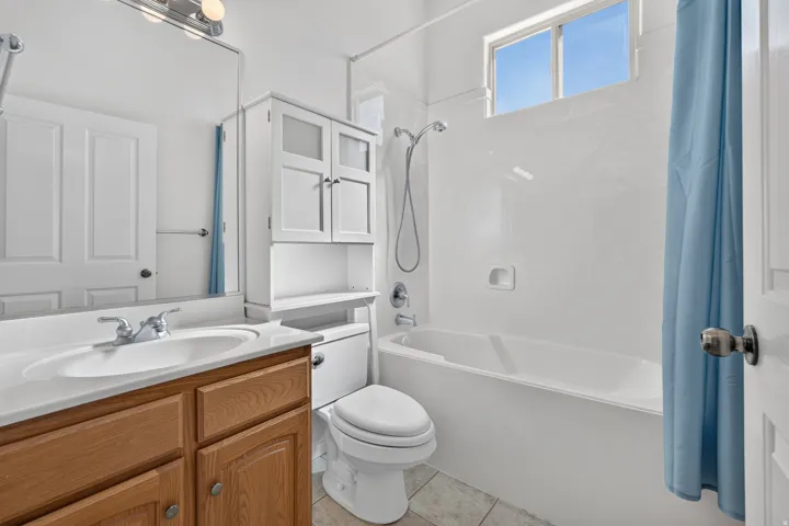 Built-in wood-finish vanity with an integrated sink and chrome faucet, white over-toilet storage cabinetry, and a bathtub with a shower fixture