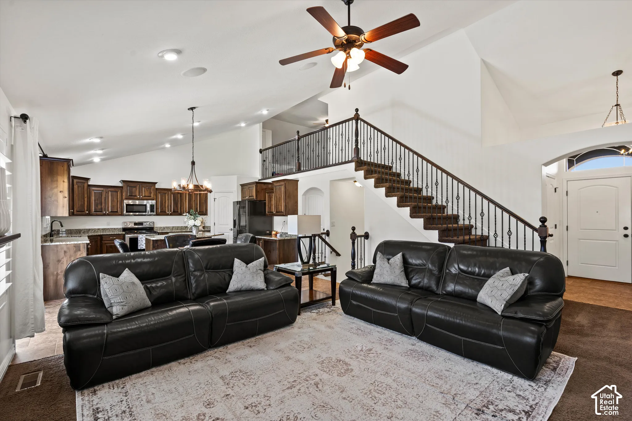 Vaulted ceilings, a dark wood-finish staircase with wrought iron balusters, a well-appointed kitchen with dark wood cabinetry, and a ceiling fan