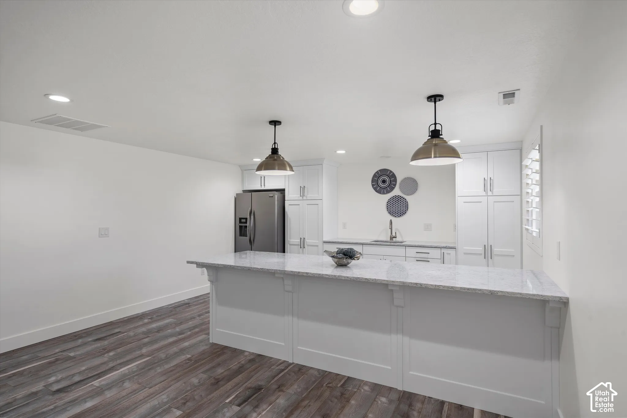 Kitchen featuring a central island with a light-toned countertop, white cabinetry, stainless steel appliances, and wood-finish flooring
