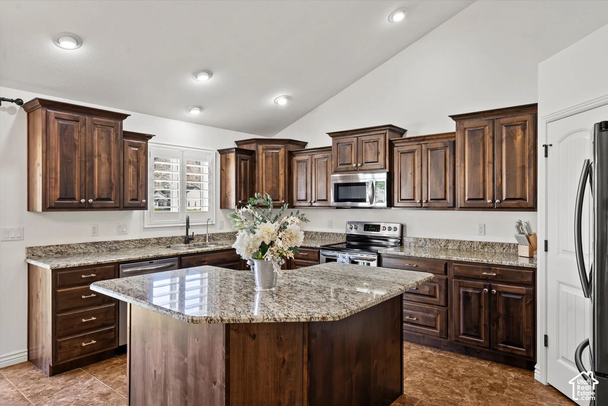 Vaulted ceiling kitchen with wood cabinetry, granite countertops, and stainless steel appliances
