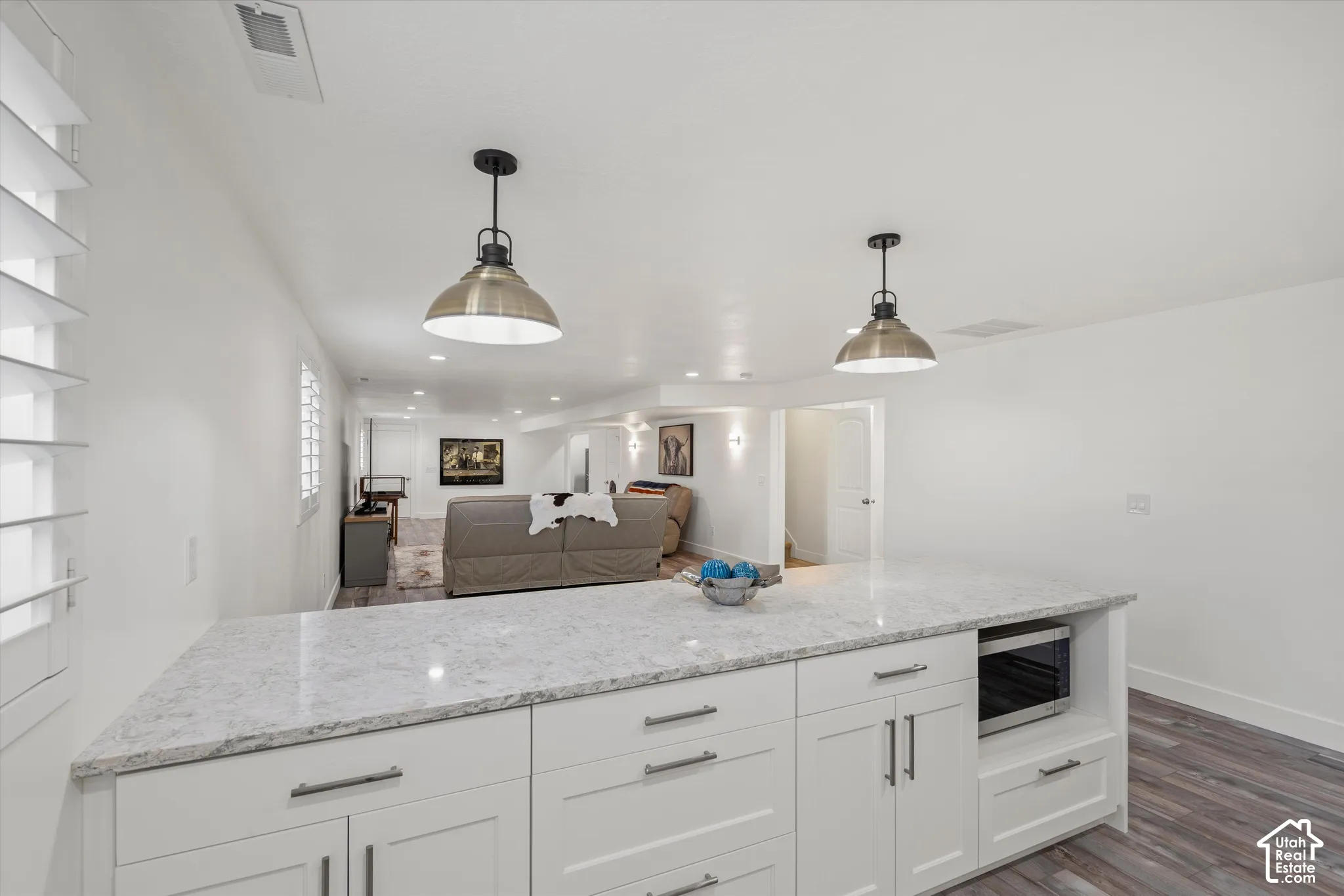 White cabinetry with sleek hardware, light-toned countertop, built-in microwave, wood-finish flooring, and recessed lighting
