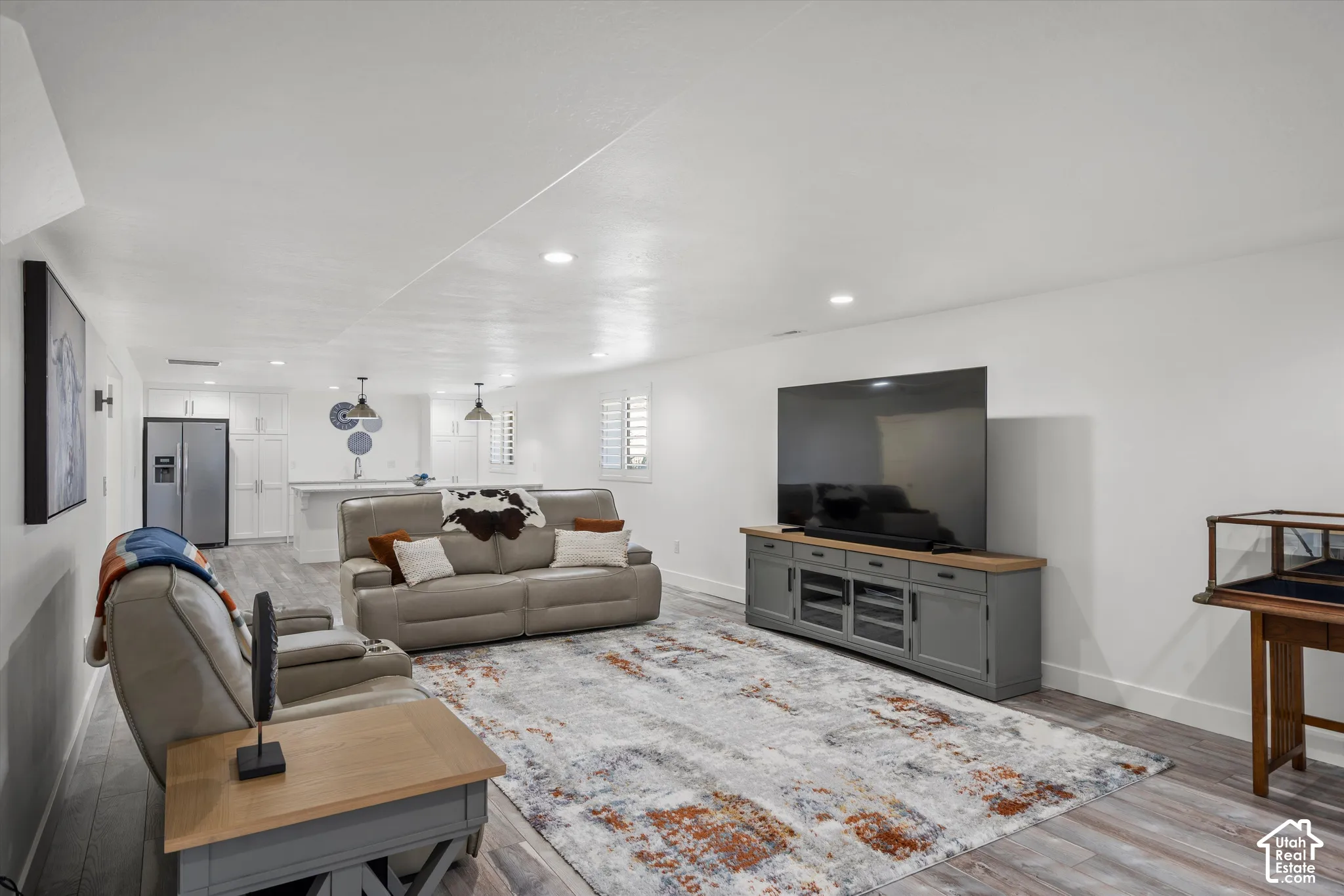 Wood-finish flooring, recessed lighting, and a kitchen area with white cabinetry, stainless steel appliances, and pendant lighting