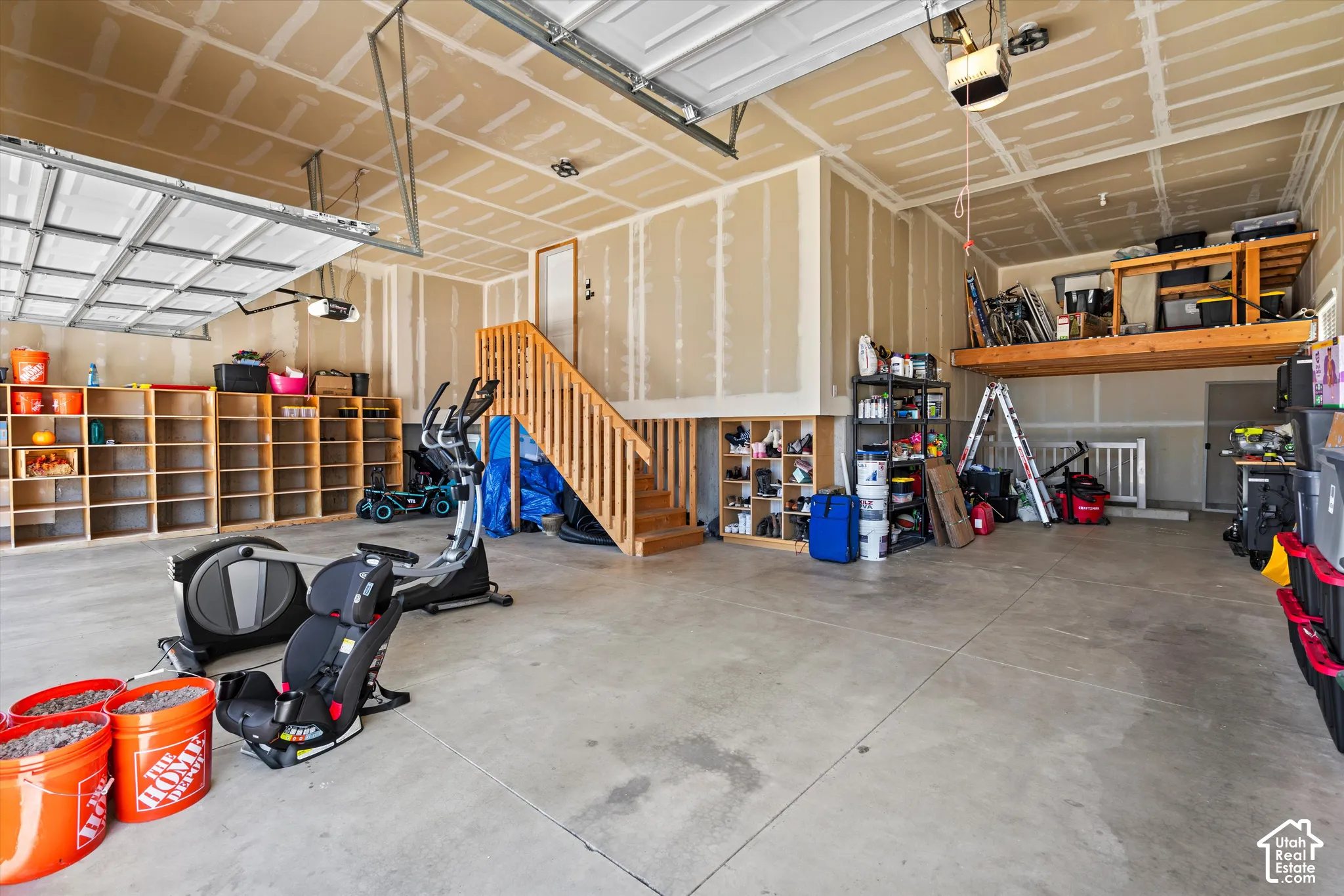 Spacious garage featuring a concrete floor, built-in wooden shelving, and an integrated wooden staircase
