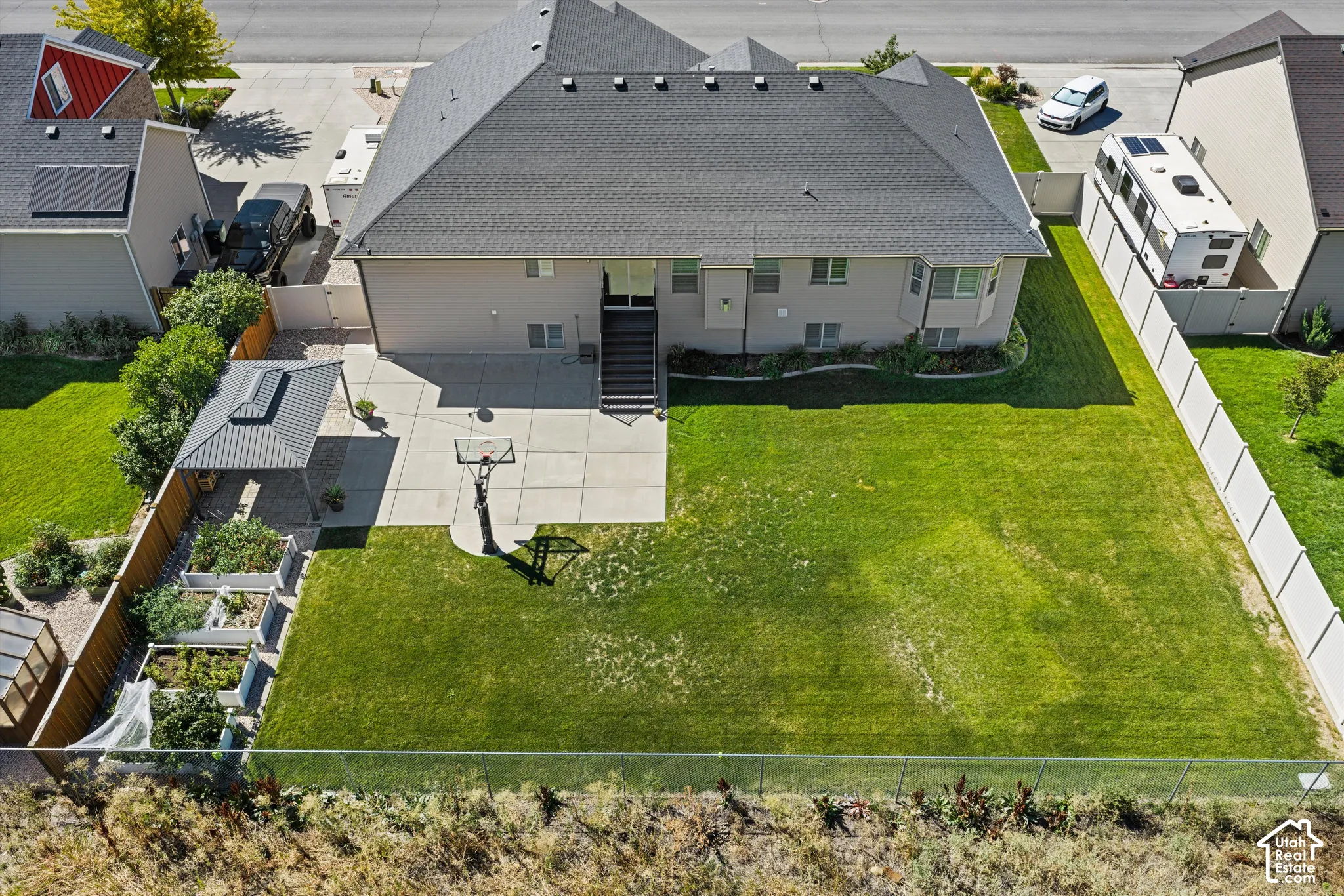 Expansive backyard featuring a large concrete patio, a basketball hoop, raised garden beds, and a covered outdoor structure