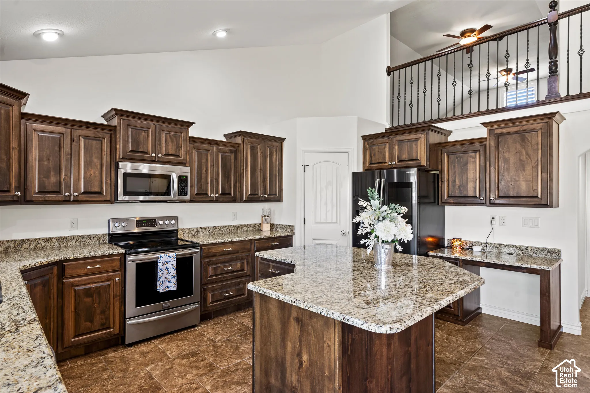 Kitchen featuring wood cabinetry, stainless steel appliances, speckled stone countertops, a central island, and tiled flooring