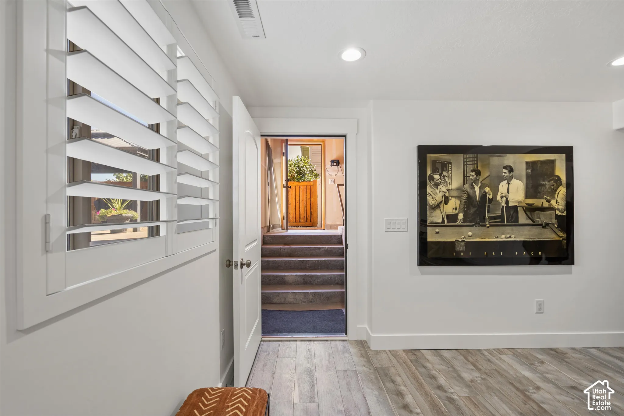 White plantation shutters, recessed ceiling lighting, wood-finish flooring, and a white interior door