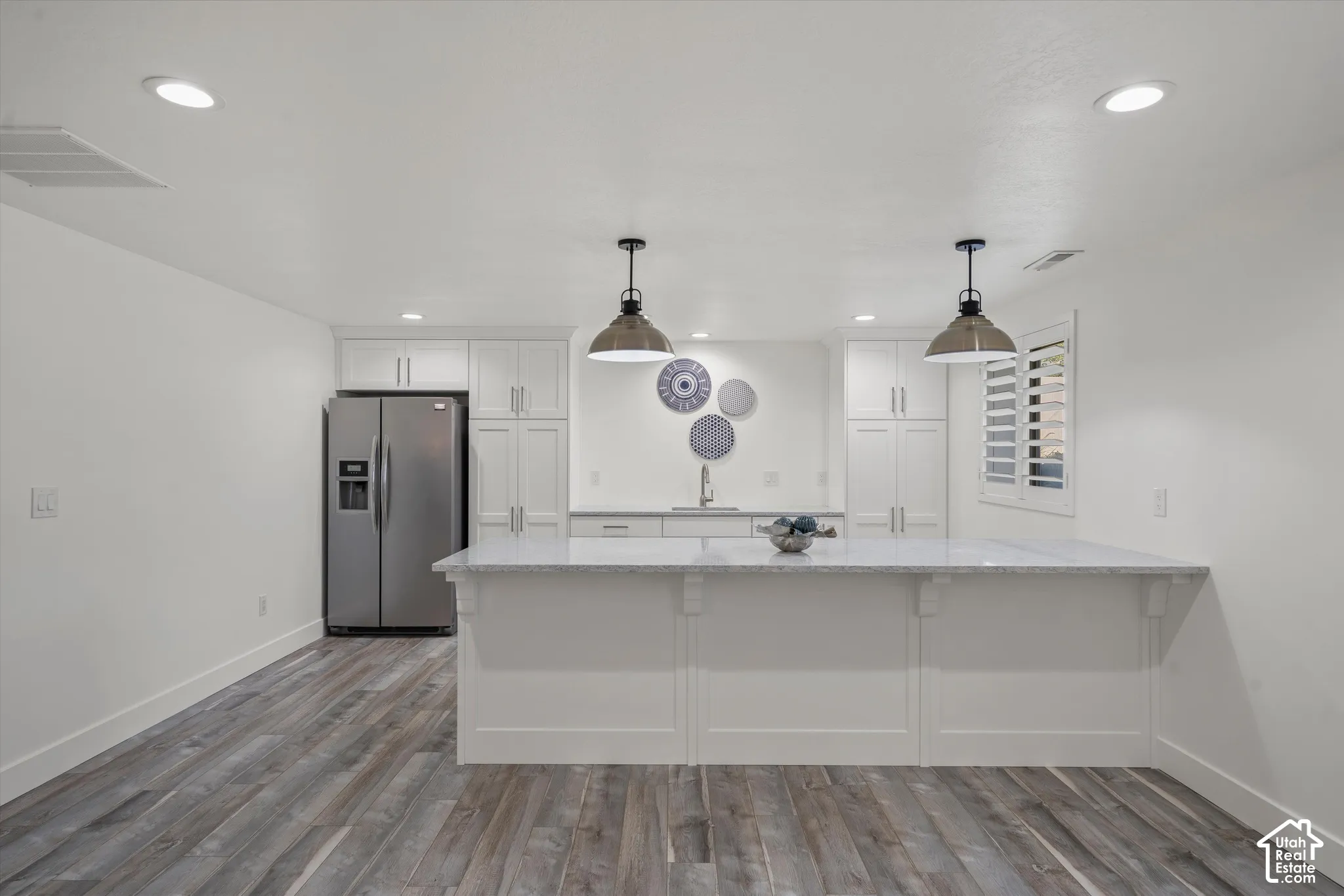 Modern kitchen featuring wood-finish flooring, recessed lighting, white cabinetry, a built-in stainless steel refrigerator, and a kitchen island with pendant lighting