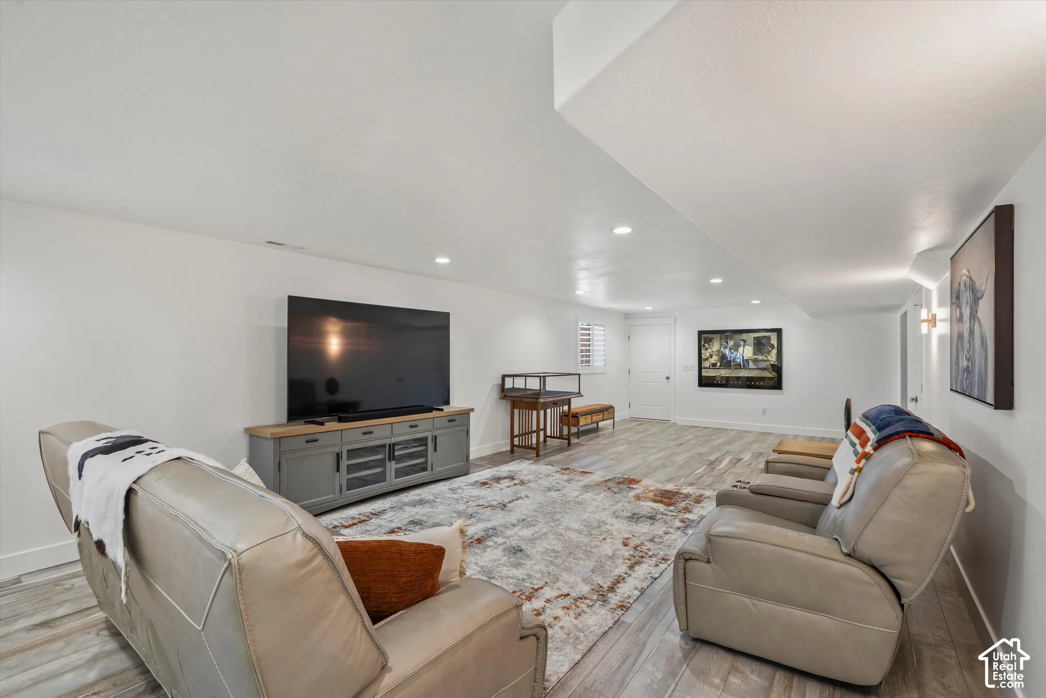 Recessed ceiling lighting, wood-finish flooring, white walls, built-in media console, and a white interior door