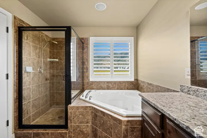 Tiled shower with a glass enclosure, corner soaking tub, and a window with plantation shutters