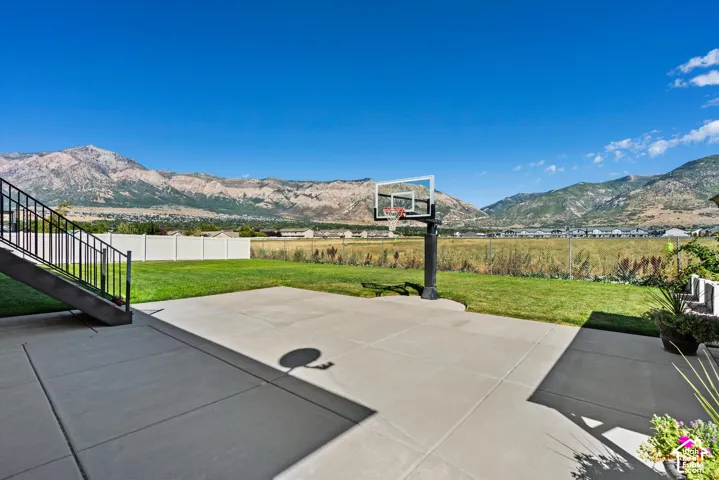 Expansive concrete patio with a basketball hoop, surrounded by a manicured lawn and a white privacy fence