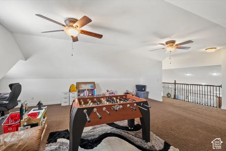 Carpeted loft area with sloped ceilings, two ceiling fans with integrated lighting, and a dark metal railing overlooking a lower level