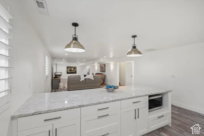 White cabinetry with sleek hardware, light-toned countertop, built-in microwave, wood-finish flooring, and recessed lighting