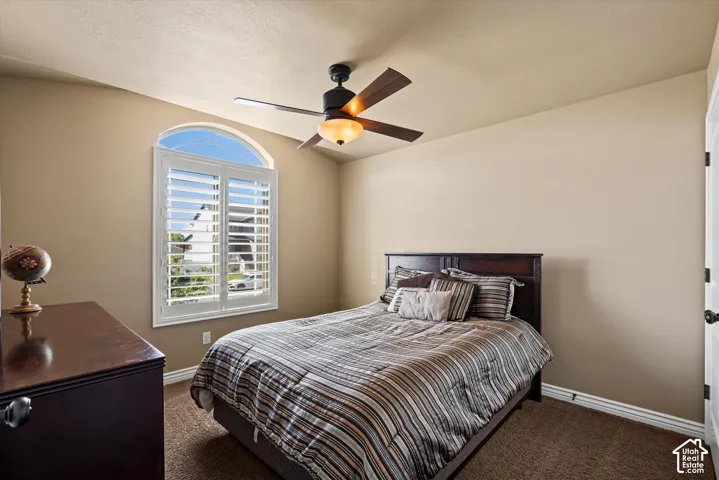 Arched window with plantation shutters, ceiling fan with integrated lighting, textured wall finishes, and dark-finish flooring