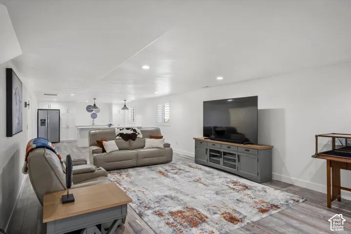 Wood-finish flooring, recessed lighting, and a kitchen area with white cabinetry, stainless steel appliances, and pendant lighting