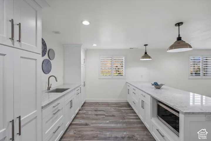 White shaker cabinetry, wood-finish flooring, undermount sink, recessed lighting, and a built-in microwave