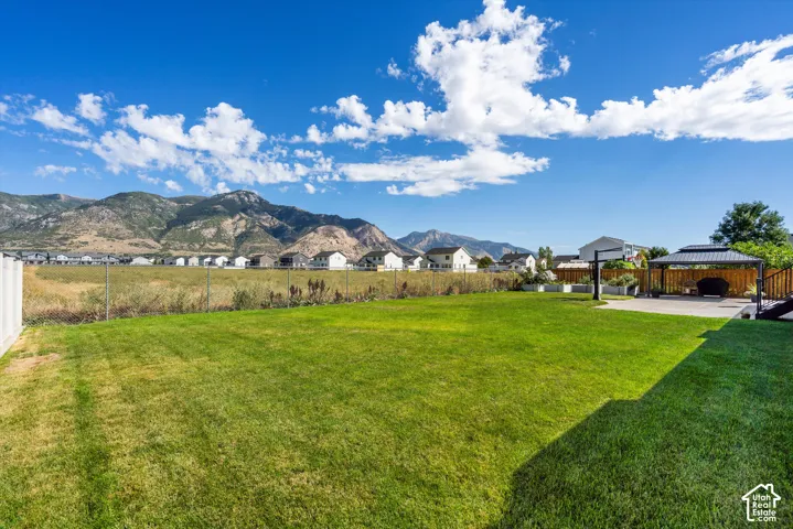 Expansive lawn area with a chain-link fence, a paved patio with a gazebo, and a mountain backdrop