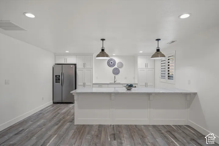Modern kitchen featuring wood-finish flooring, recessed lighting, white cabinetry, a built-in stainless steel refrigerator, and a kitchen island with pendant lighting