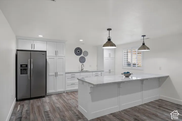 Modern kitchen featuring white cabinetry, a stainless steel side-by-side refrigerator, a kitchen island with pendant lighting, stone countertops, and wood-finish flooring