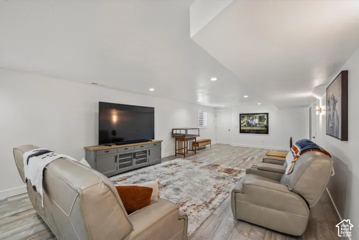 Recessed ceiling lighting, wood-finish flooring, white walls, built-in media console, and a white interior door