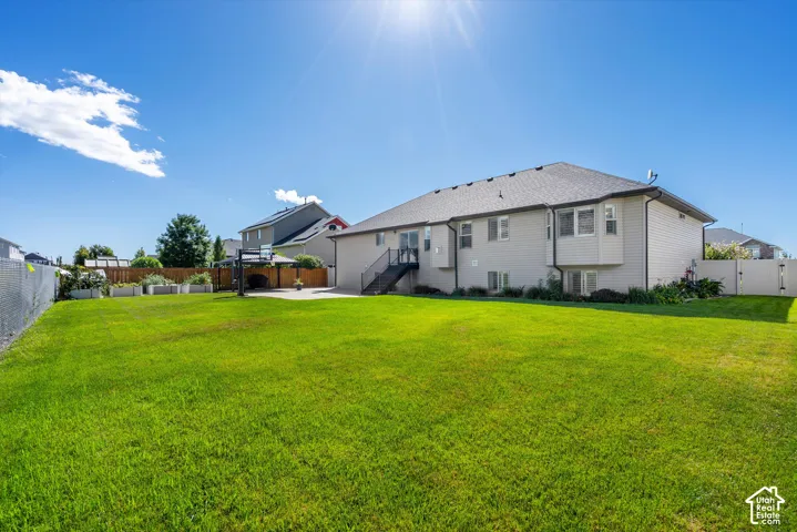 Expansive green lawn, fenced perimeter, rear deck with black railings, lower-level windows, and a raised planter garden