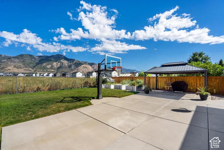 Expansive concrete patio with a basketball hoop, covered metal gazebo, and a manicured lawn