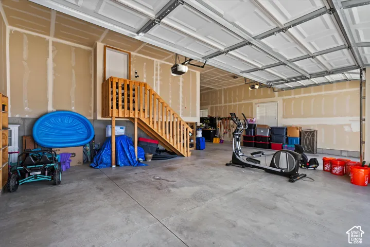Spacious garage with concrete flooring, overhead garage doors, and natural wood staircase leading to an upper level