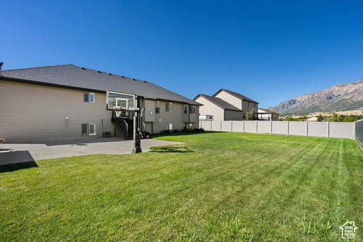 Expansive grassy yard with concrete patio, full privacy fencing, and mountain backdrop