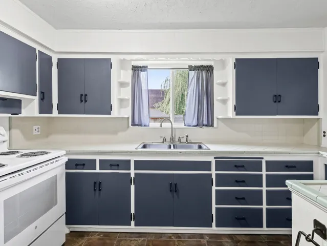 Two-tone cabinetry with black hardware, tile countertops, stainless steel sink, and a white electric range